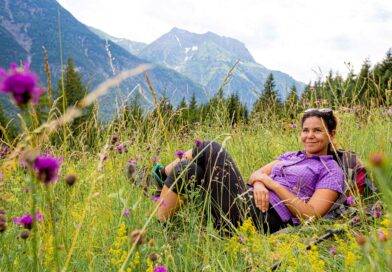Frau in lila Hemd entspannt auf einer Blumenwiese in den Allgäuer Alpen – ideale Umgebung für eine freie Taufe im Allgäu