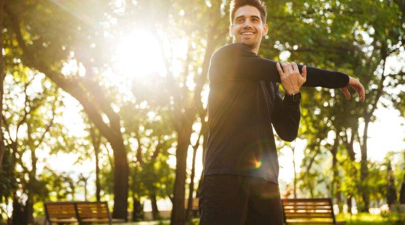 mann beim dehnen im park in koeln, mit sonnenschein im hintergrund, waehrend eines outdoor-fitness-trainings mit personal trainer aus koeln