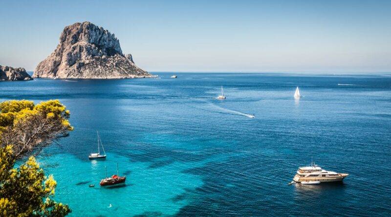 Türkisblaues Meer mit Segelbooten und luxuriöser Yacht vor der Küste Ibizas, im Hintergrund der imposante Felsen Es Vedrà – idealer Ort für Beach Restaurants Ibiza.