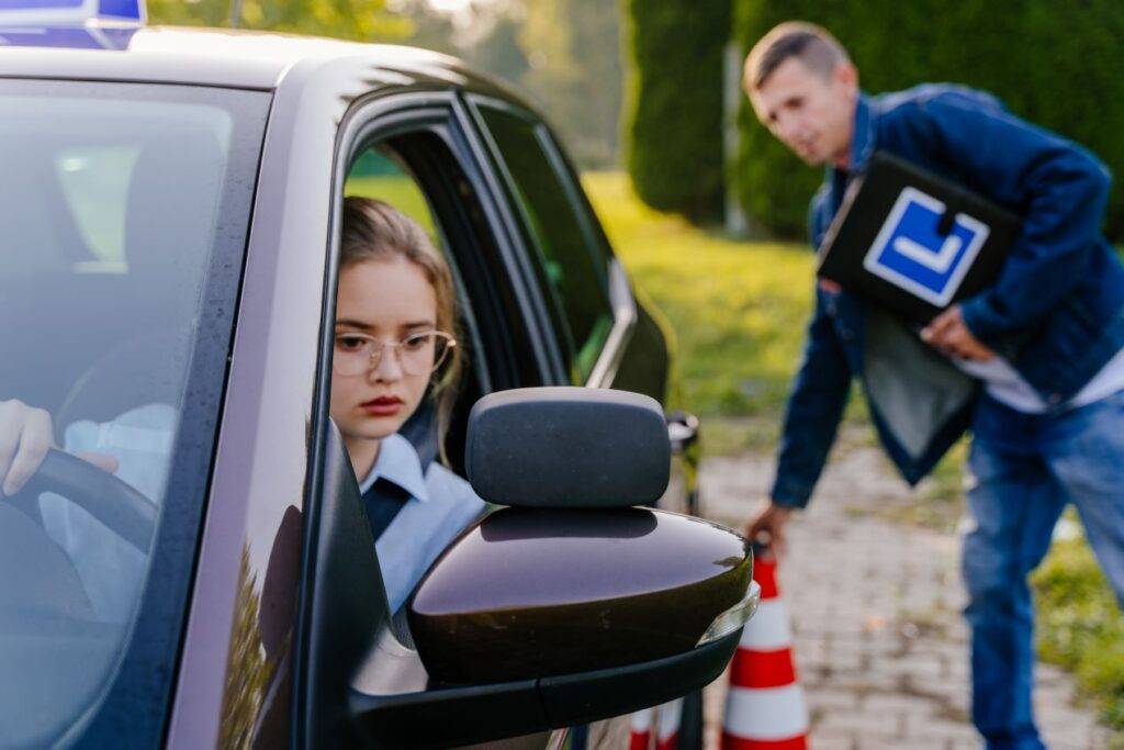 Junge Fahrschülerin konzentriert sich auf das Einparken während einer Fahreinheit, betreut von einem Fahrlehrer mit Verkehrshütchen.