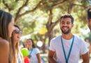 Eine Gruppe von lachenden Menschen bei einer Outdoor-Veranstaltung, die im Grünen stattfindet, nahe einem Partyzelt mit bunten Dekorationen.