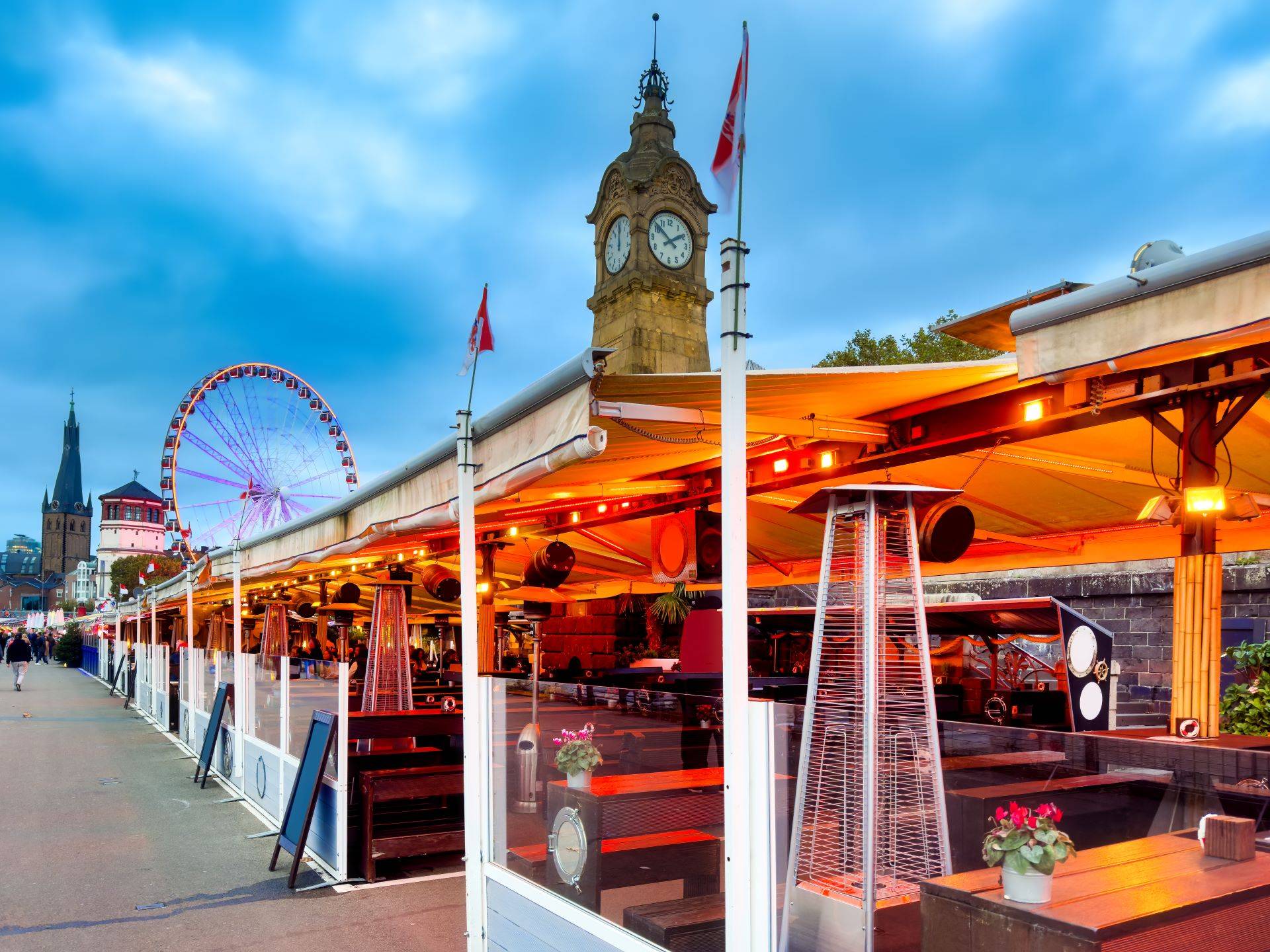 Rheinufer mit beleuchteten Restaurants und Blick auf das Riesenrad in Düsseldorf